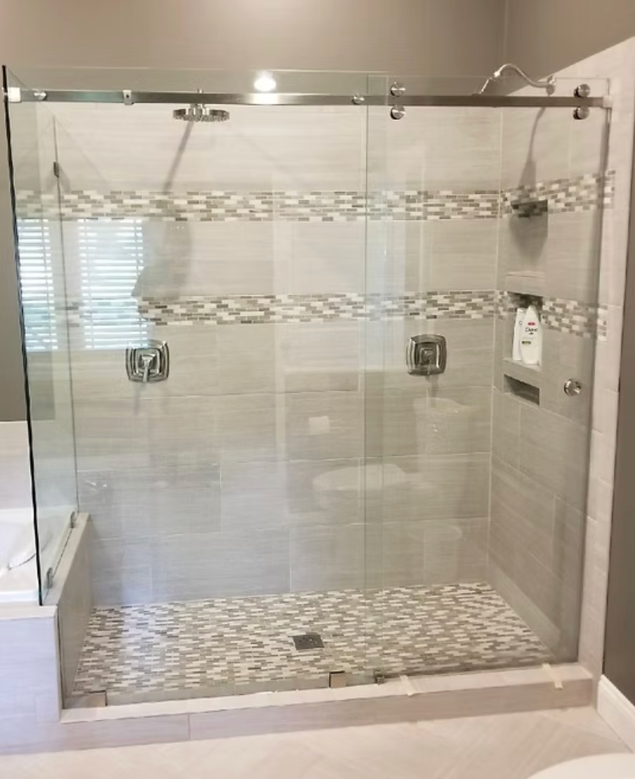 Glass shower with sliding door, light tile walls and mosaic accent, pebble floor.