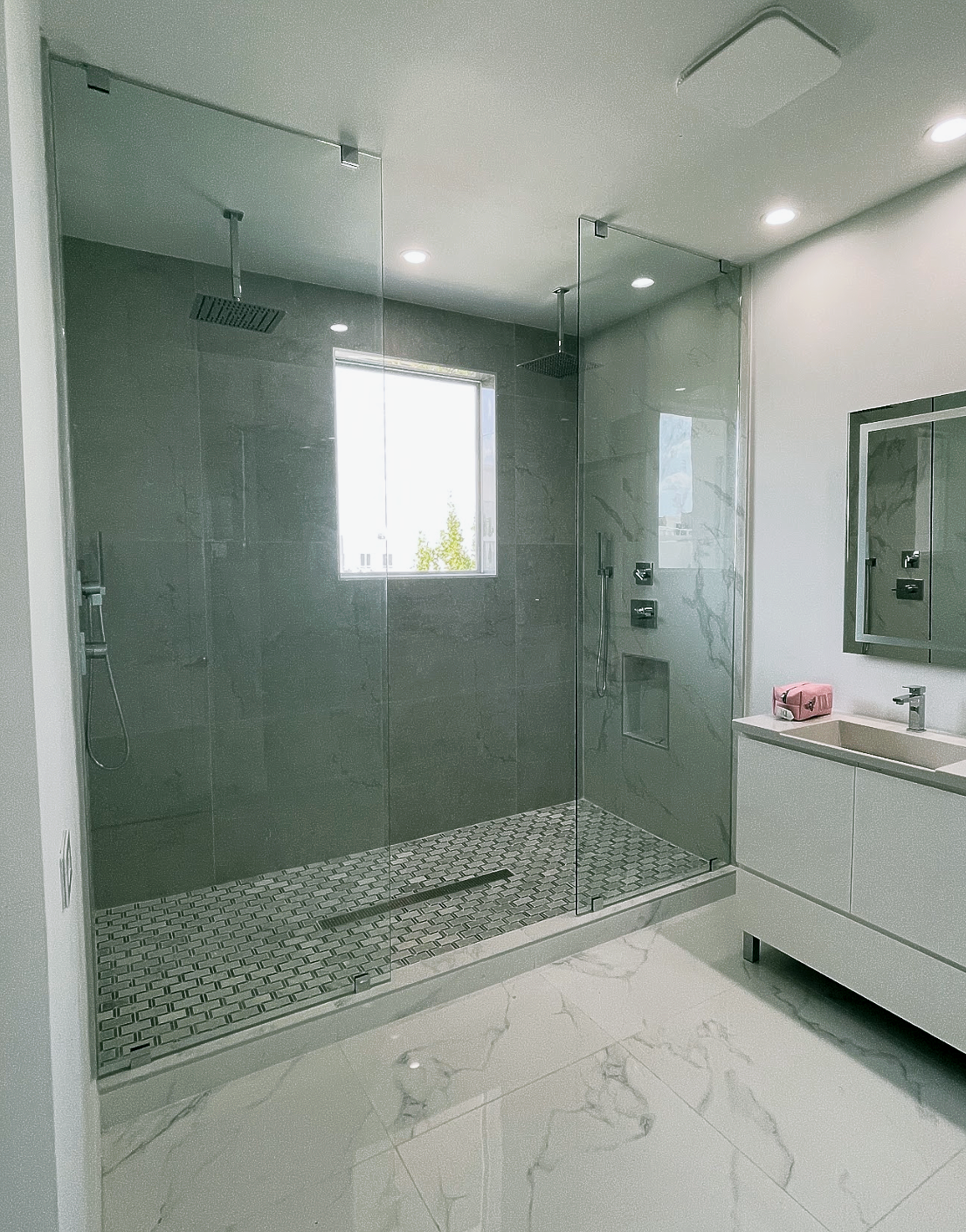 Modern bathroom with glass shower, gray tile walls, pebble floor, and white vanity.