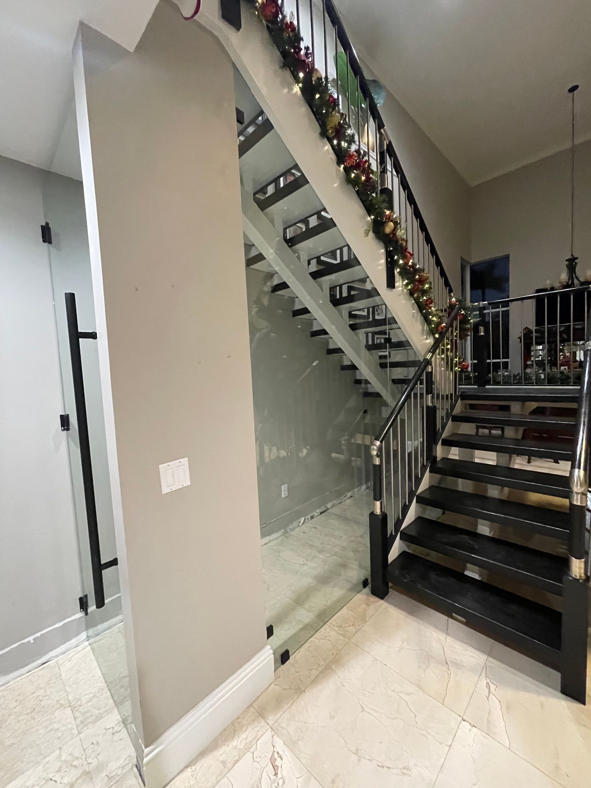 Glass enclosure under stairs with wreath hanging over the handrail.