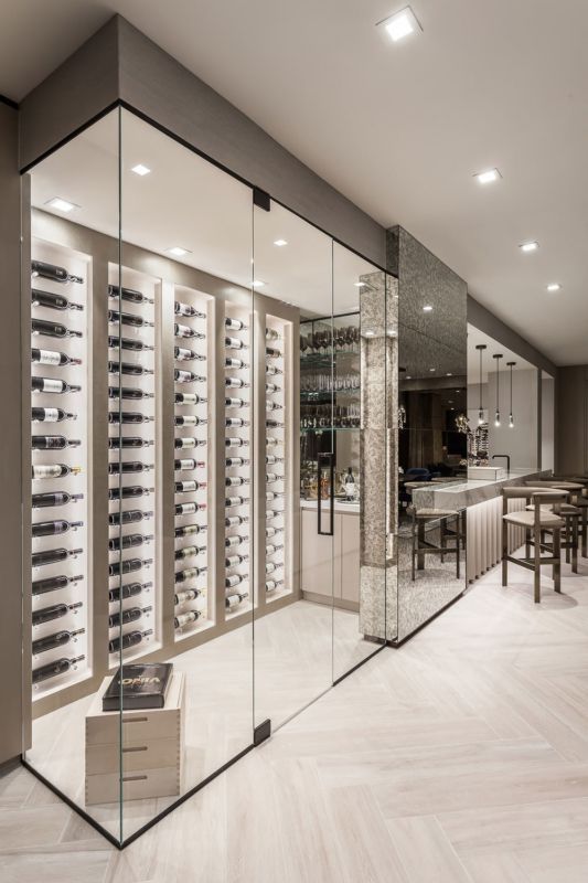 Modern wine cellar with glass walls displaying bottles, leading to a bar area with stools and a textured wall.