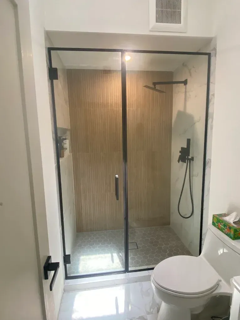 Cabina de ducha de vidrio con panel fijo y acabado en negro instalada en West Kendall.