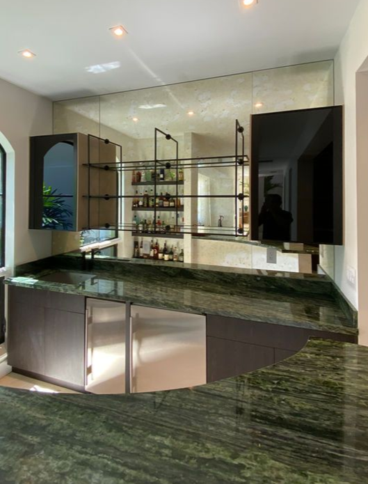 Wall to Wall mirror behding wood and glass cabinets with steel metals shelves over a green marble countertop.