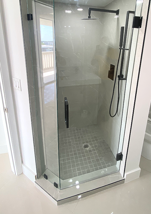 Glass shower enclosure with gray tile floor, white walls, and black fixtures.
