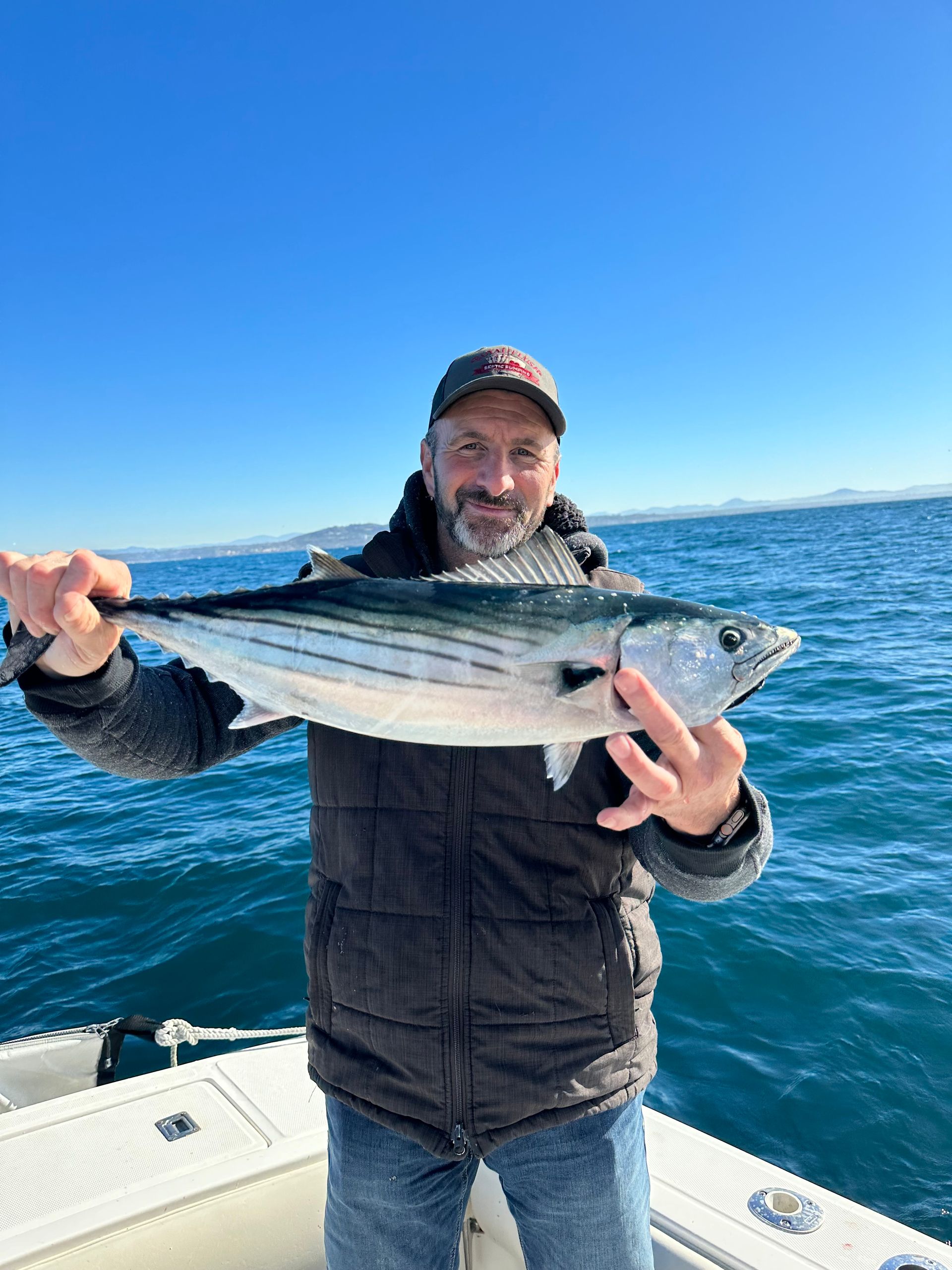 A man is holding a fish on a boat in the ocean.