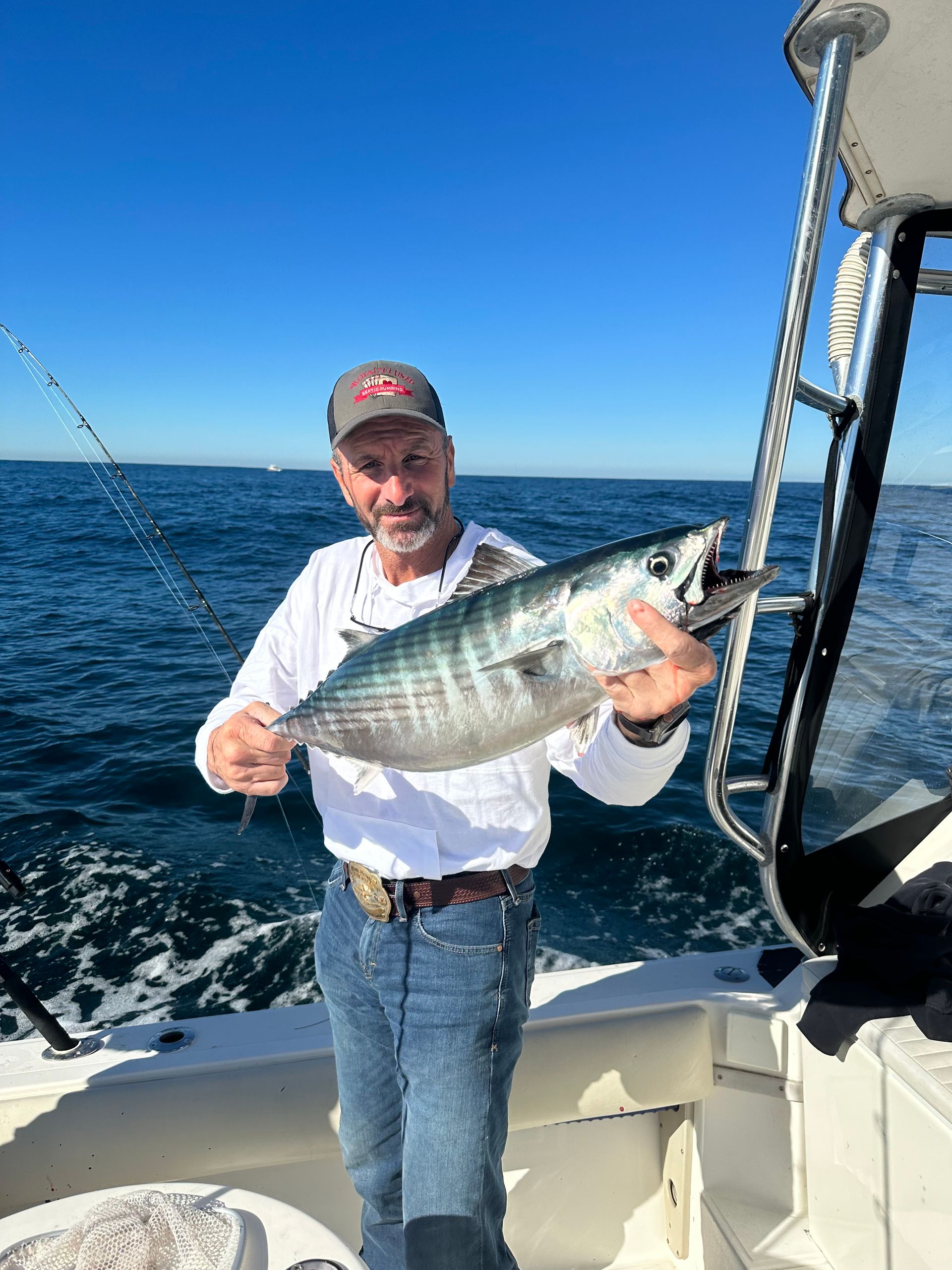 A man is holding a fish on a boat in the ocean.
