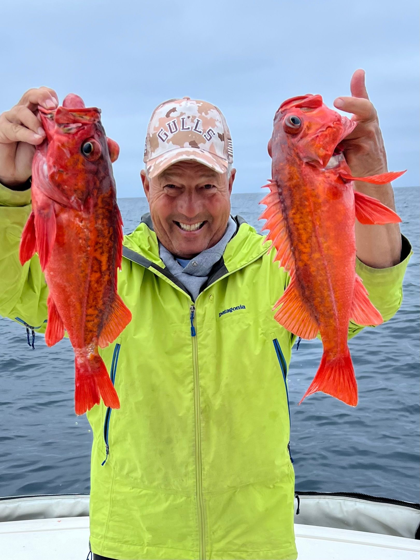 A man in a yellow jacket is holding two red fish in his hands.