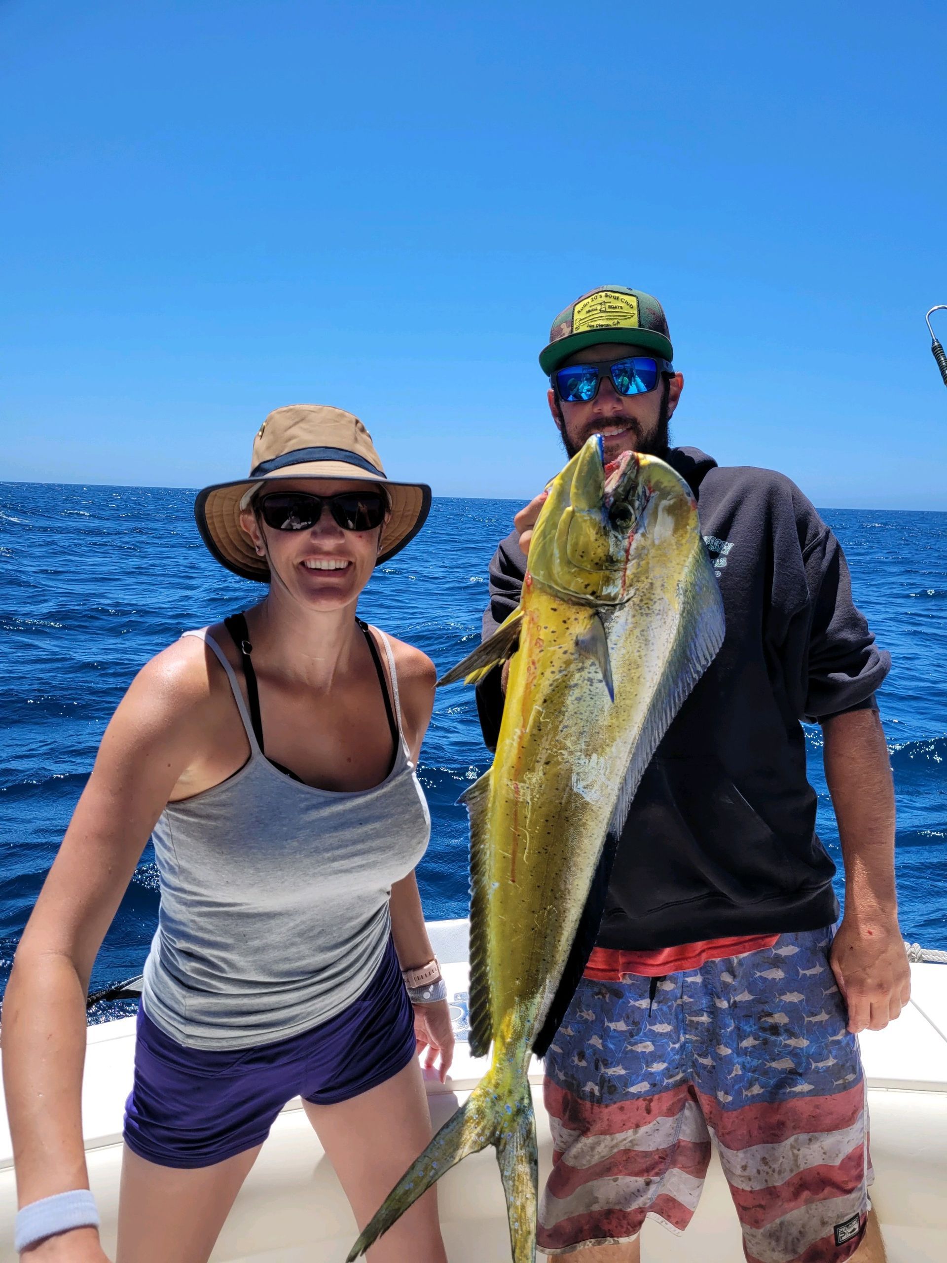 A man and a woman are standing on a boat holding a fish.
