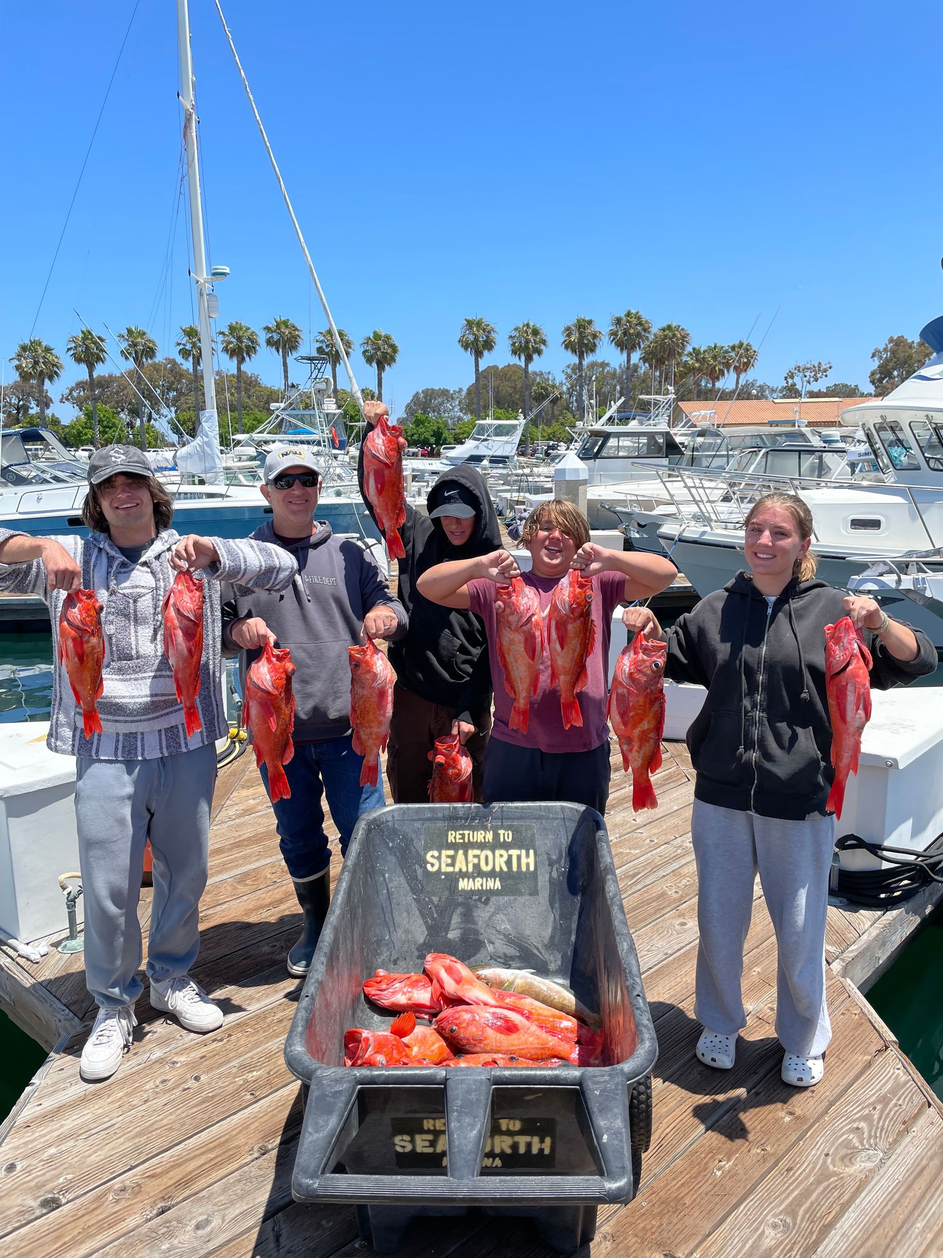 A group of people are standing on a dock holding fish.