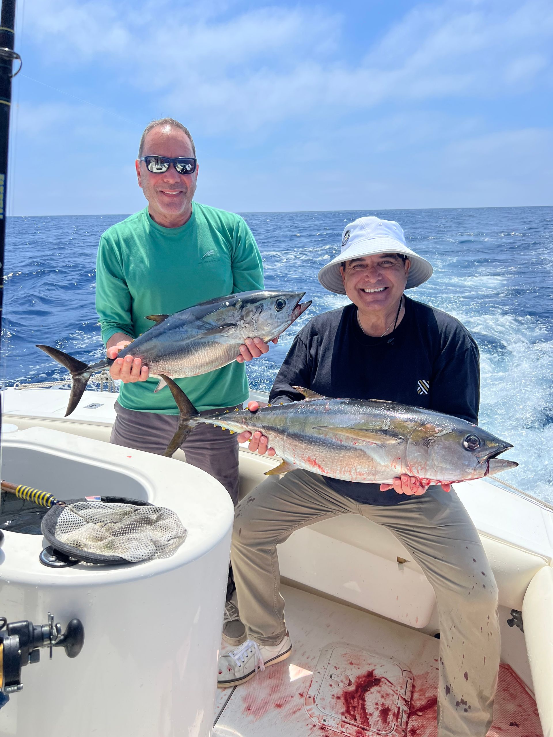 Two men are holding fish on a boat in the ocean.