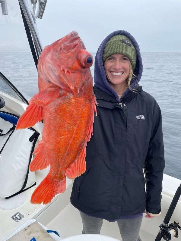 A woman is holding a large red fish on a boat