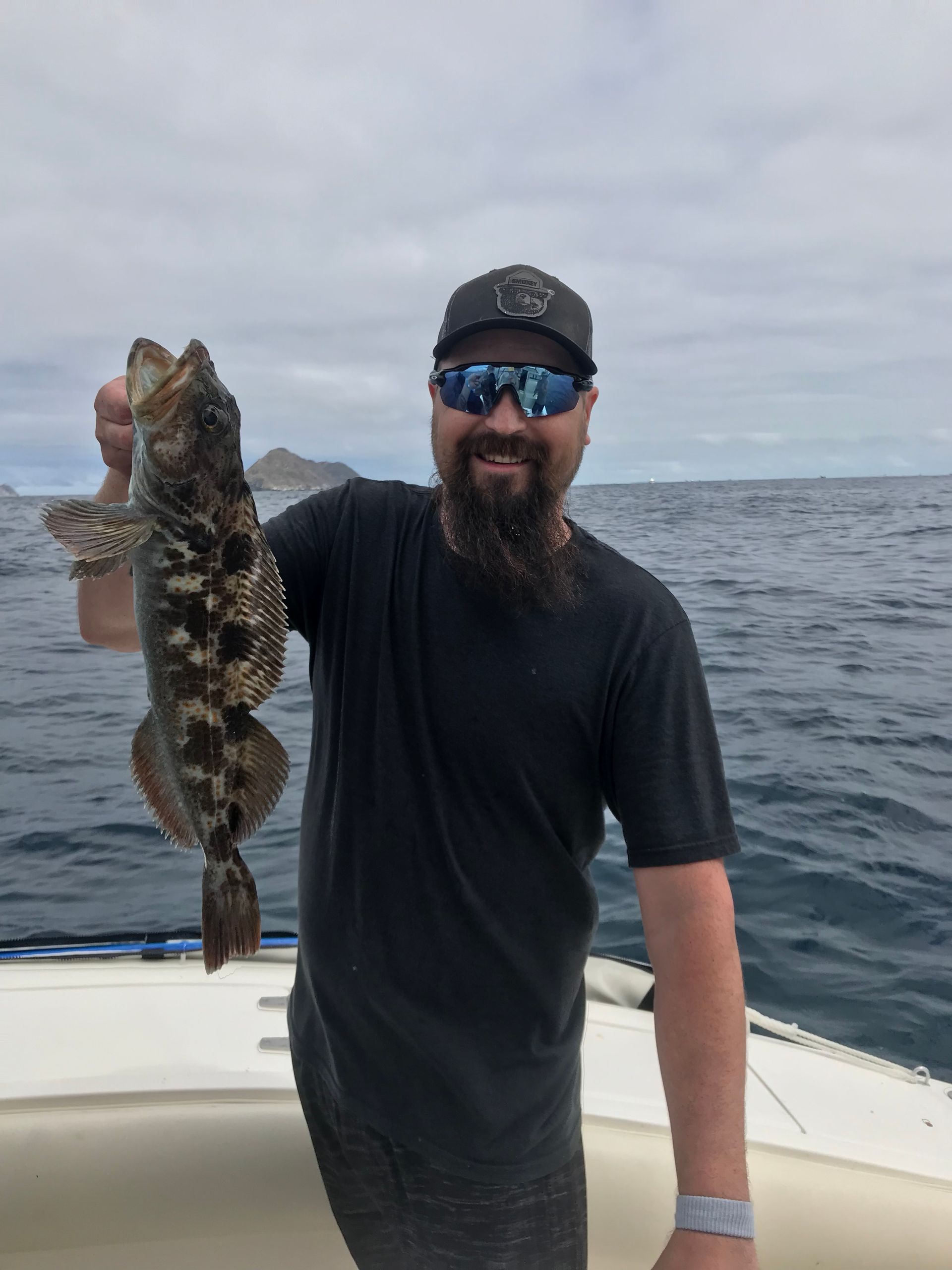 A man with a beard is holding a large fish on a boat.