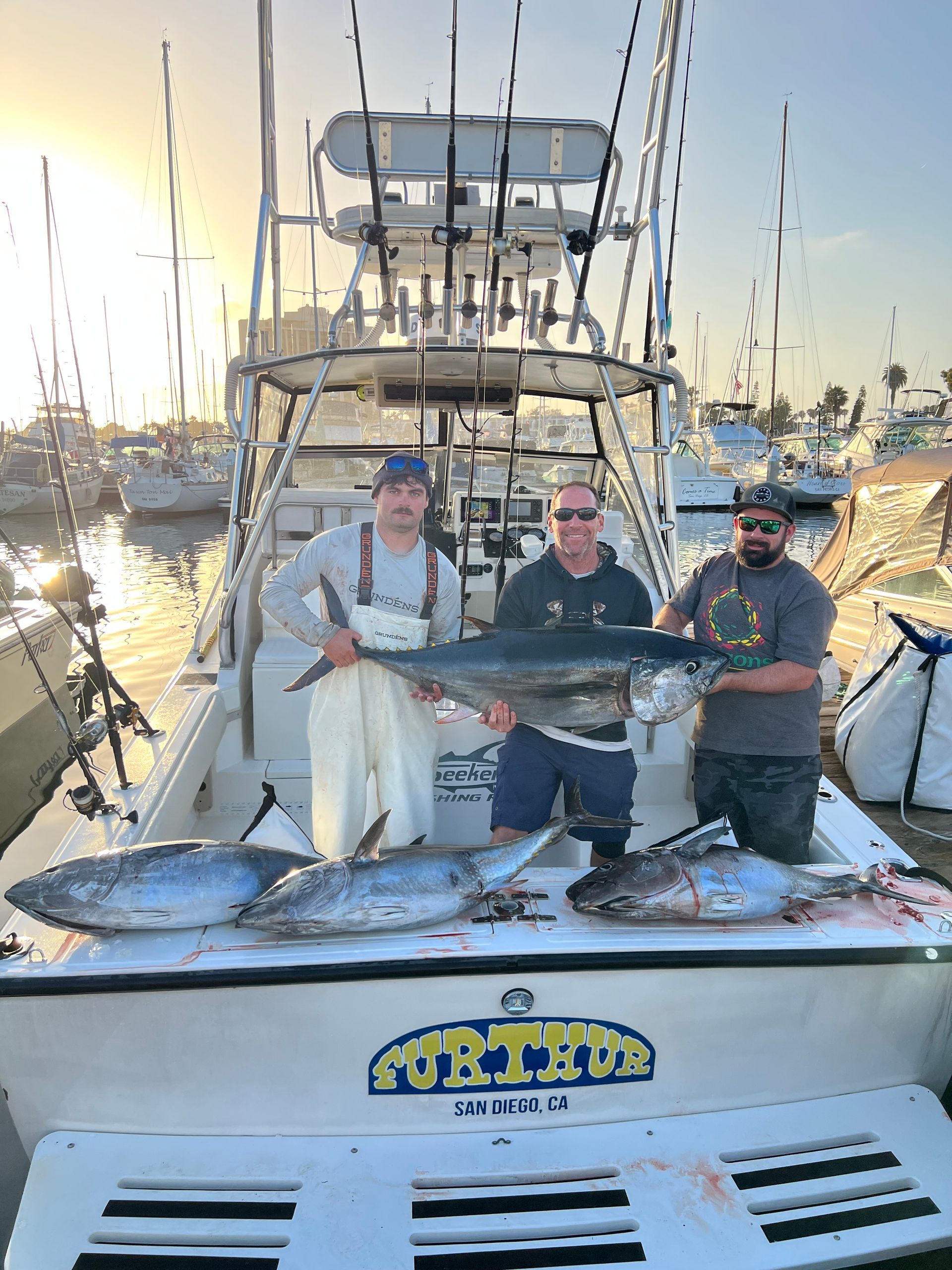 Three men are standing on a boat holding fish.