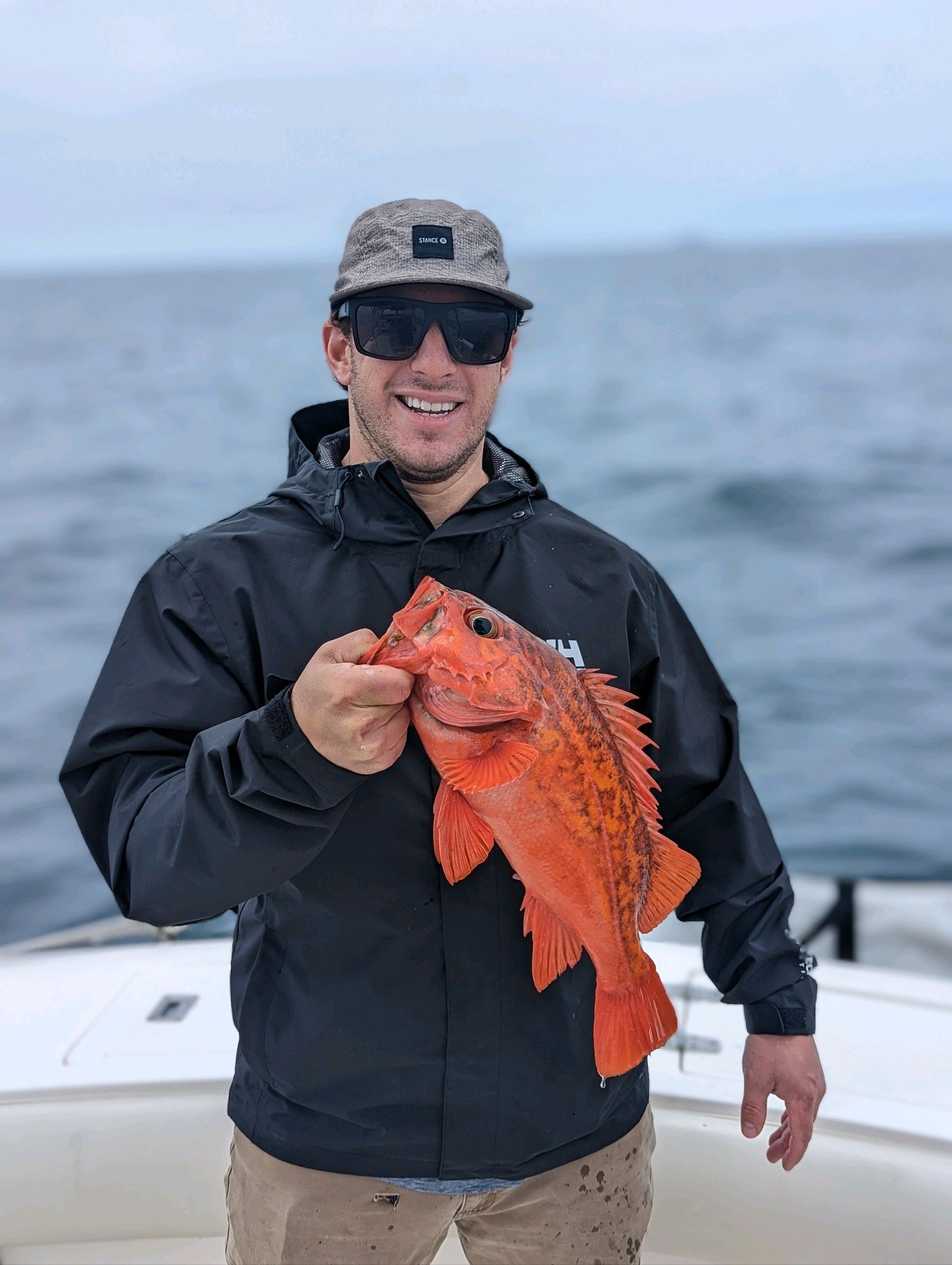 A man is holding a red fish in his hand on a boat.
