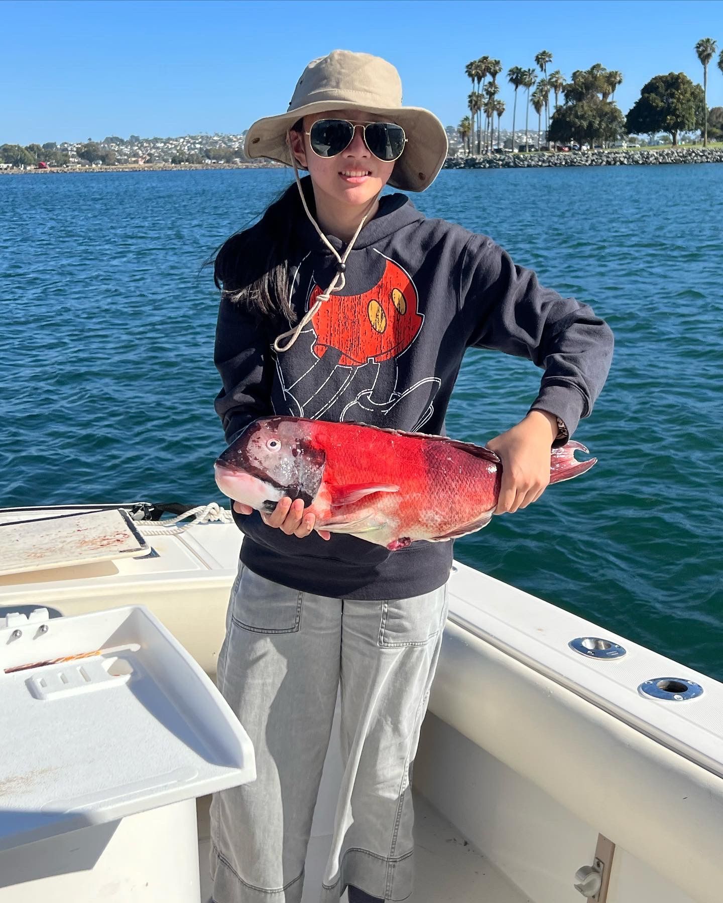A woman is holding a large red fish on a boat