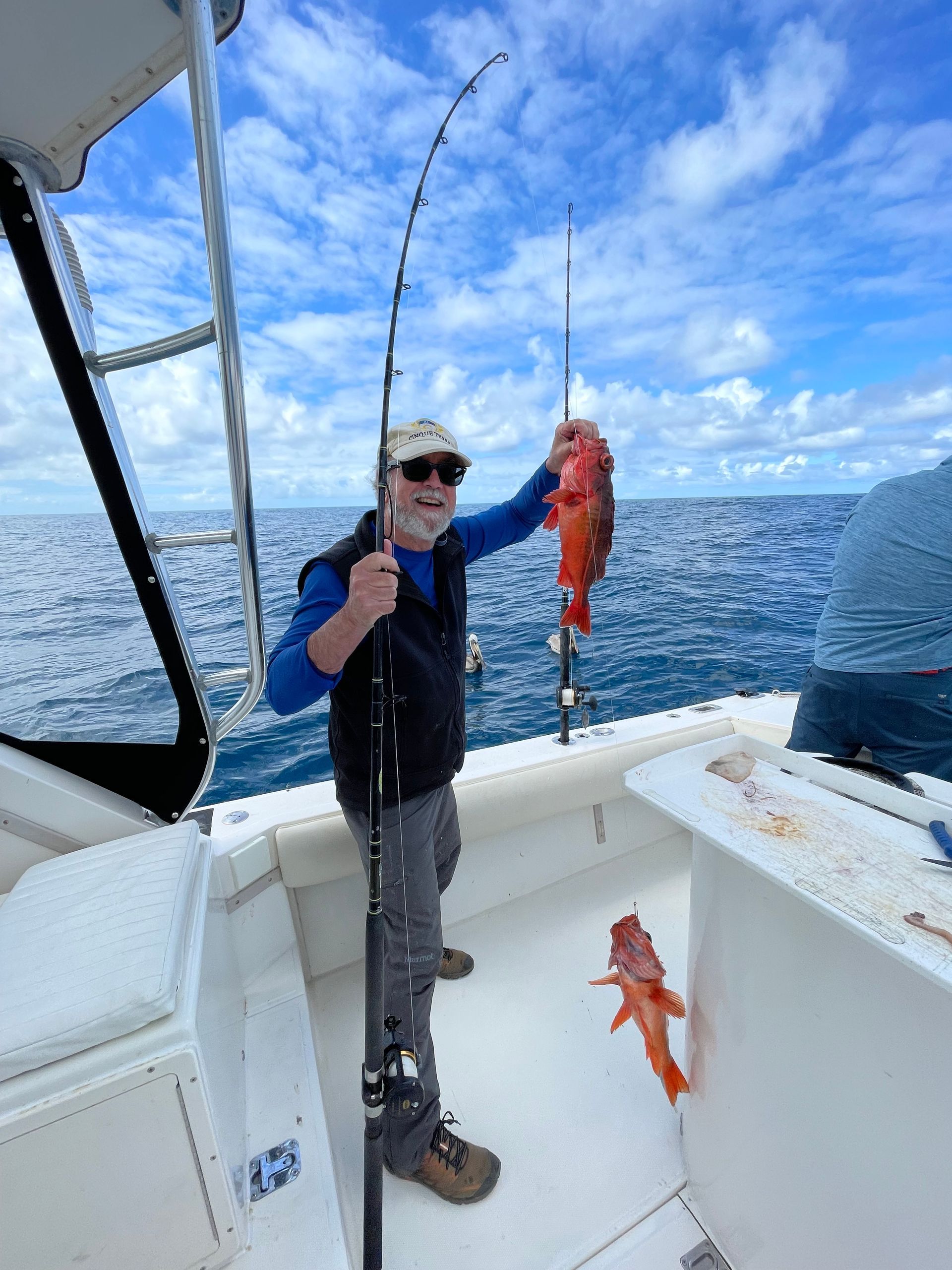 A man is standing on a boat holding a fish and a fishing rod.