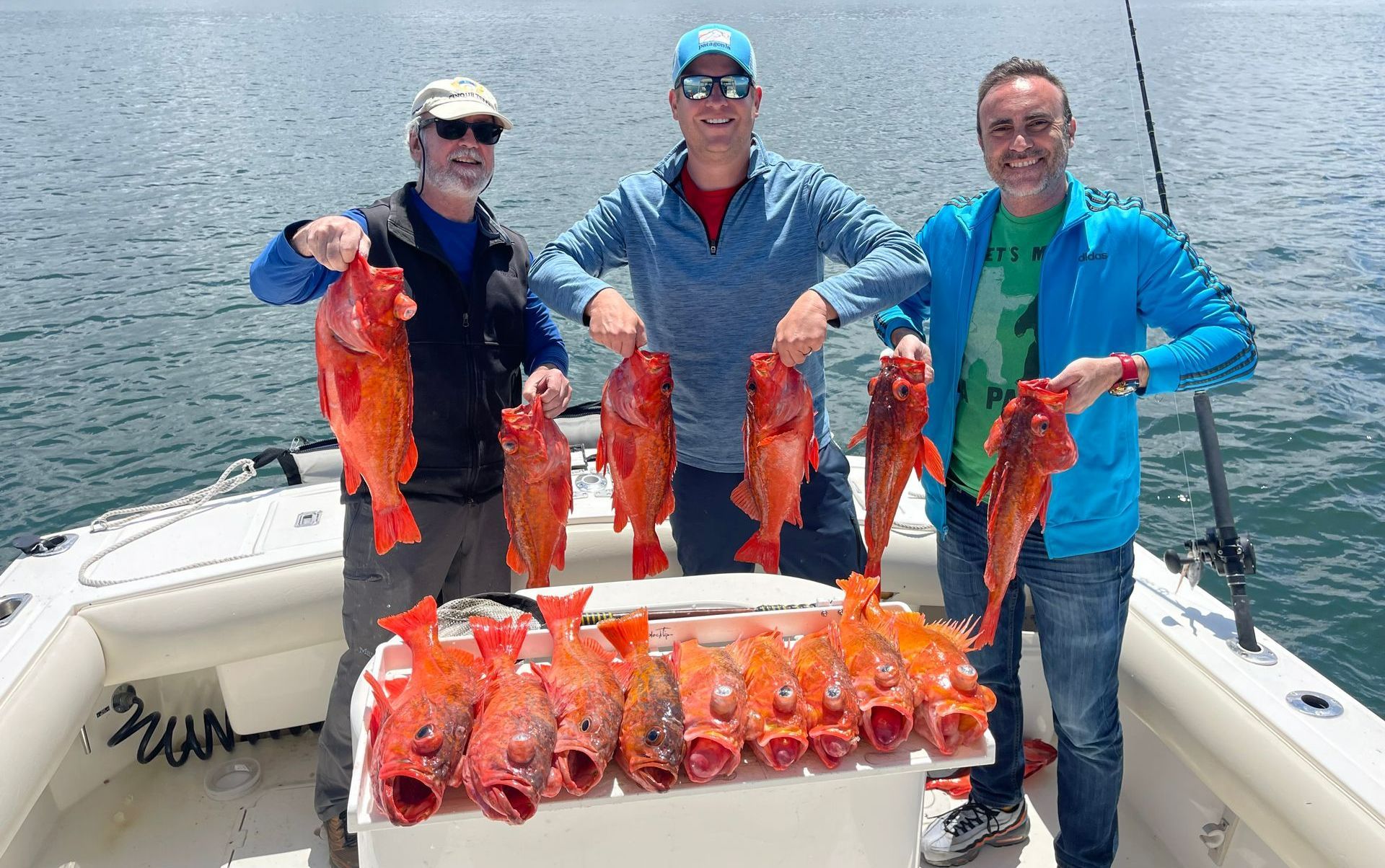 Three men are standing on a boat holding red fish.