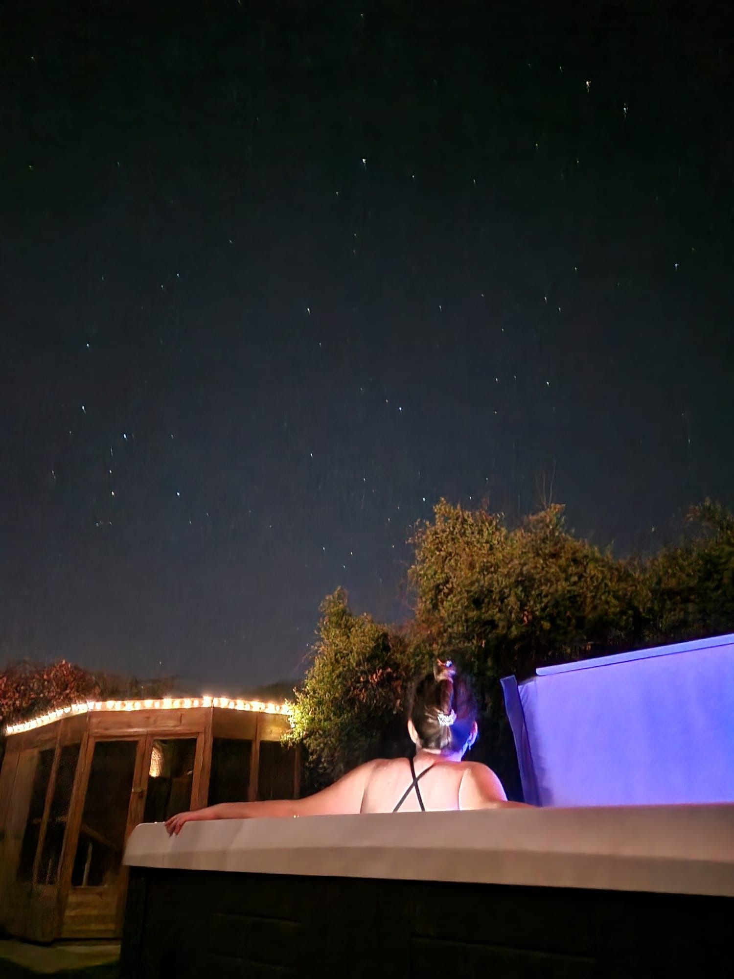 A hot tub is lit up at night in front of a brick wall.