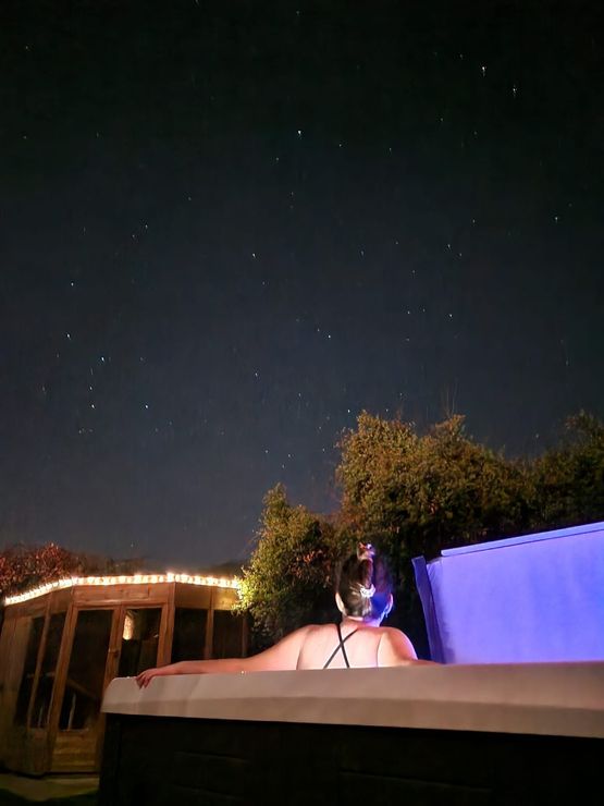 A hot tub is lit up at night in front of a brick wall.
