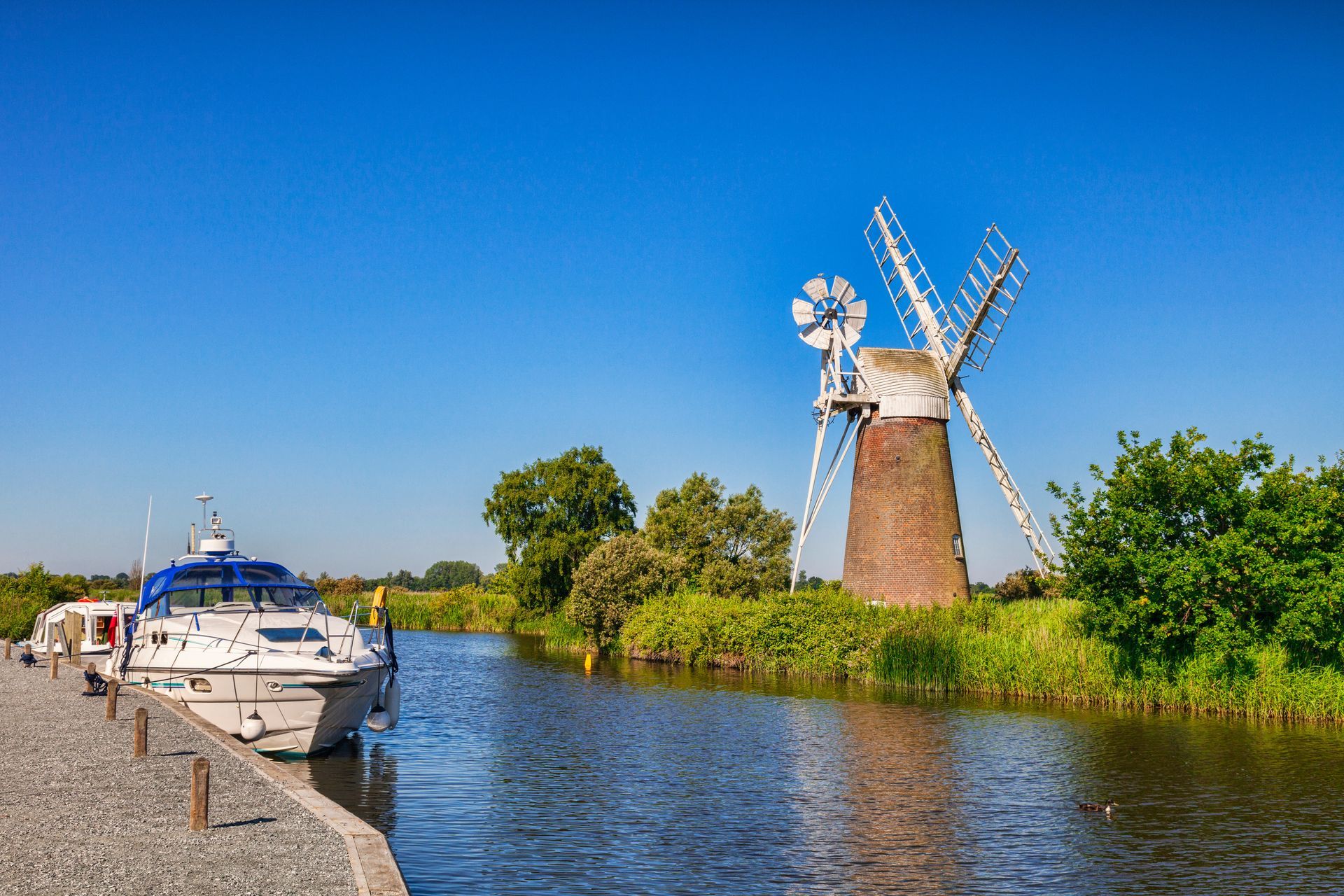 A boat is docked next to a windmill on the shore of a river.