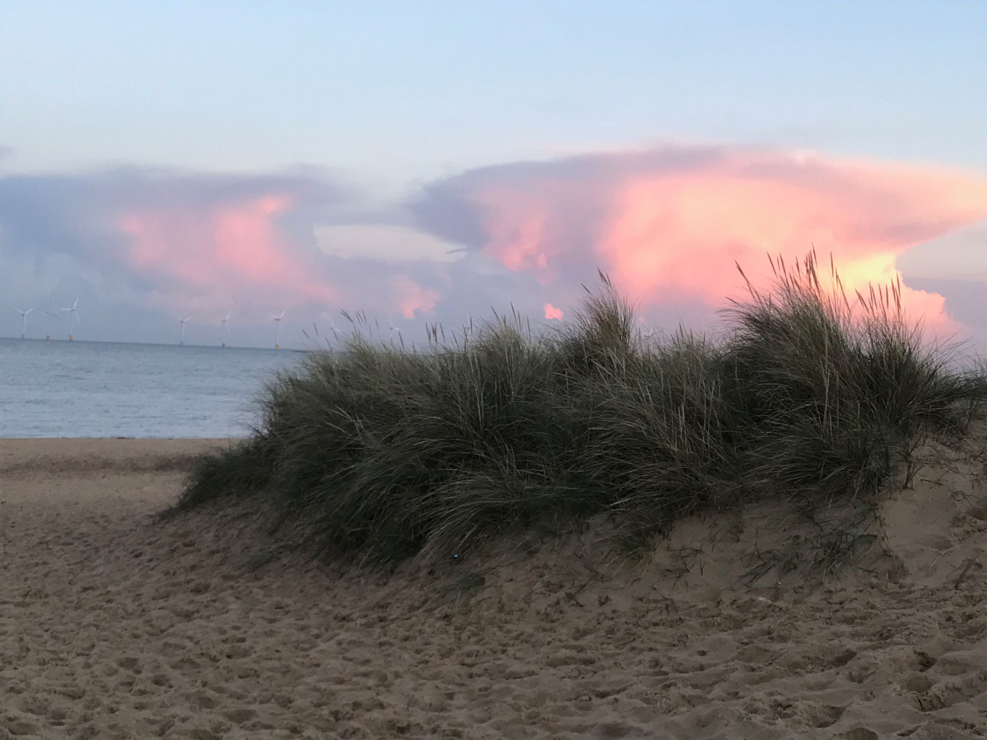 A sunset over a beach with sand dunes in the foreground.