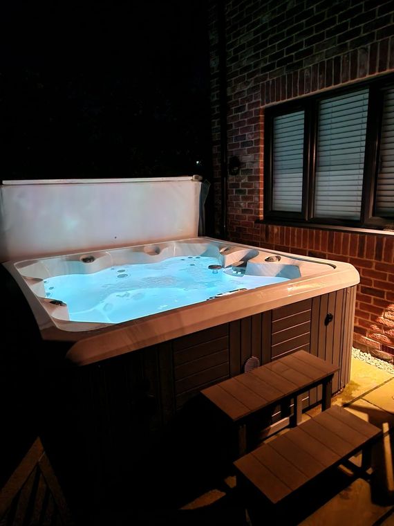 A hot tub is lit up at night in front of a brick wall.