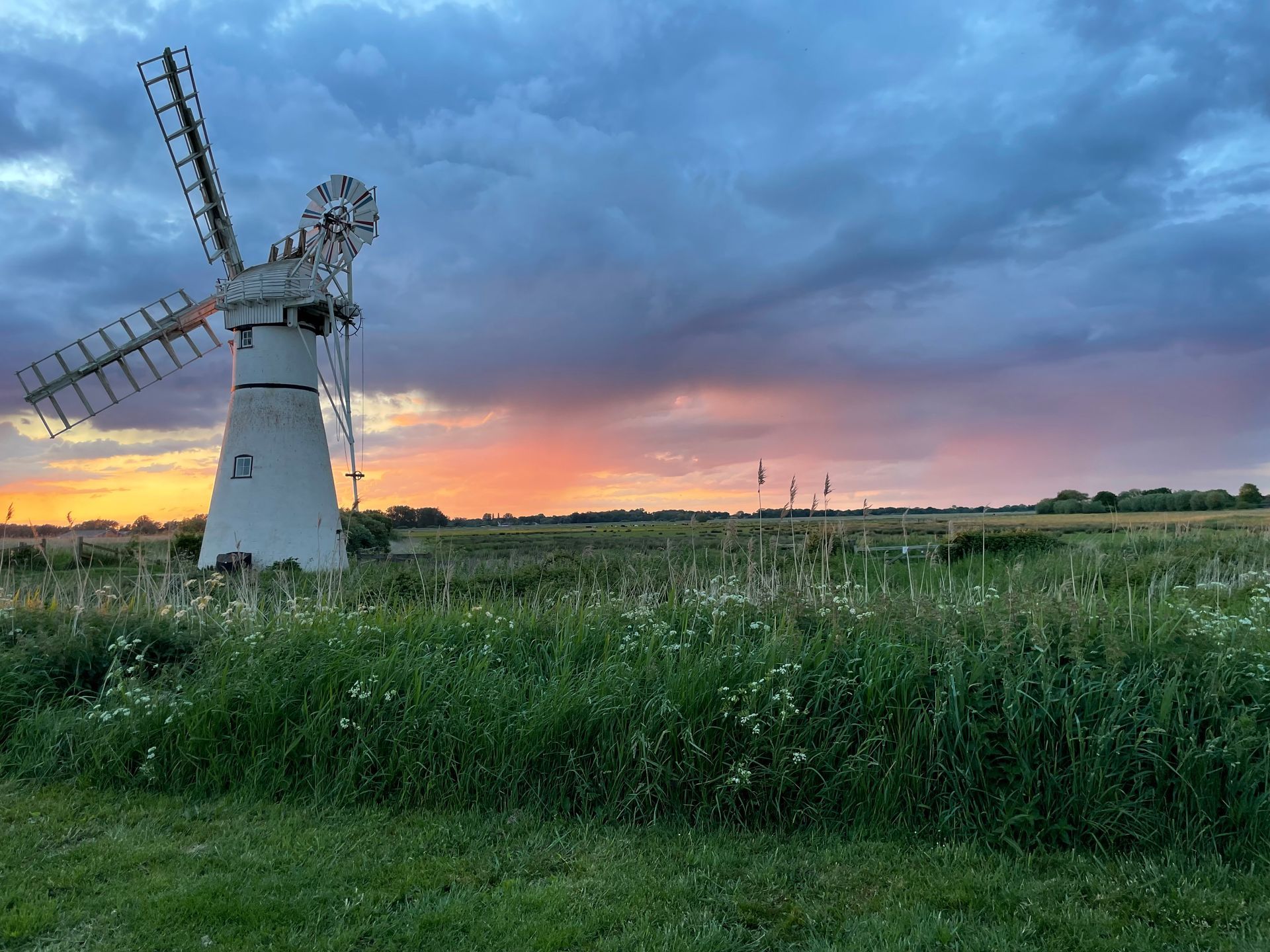 A windmill is sitting in the middle of a field at sunset.