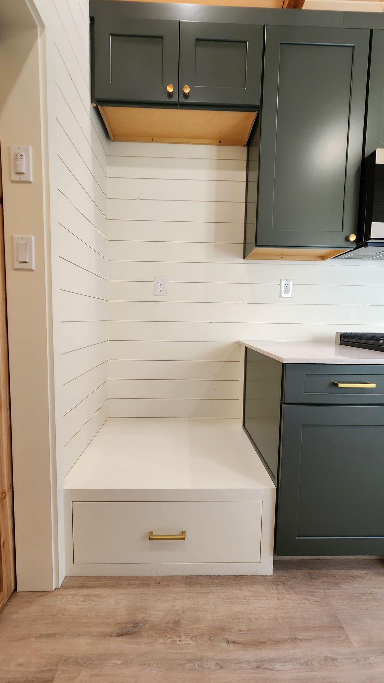 Kitchen nook with built-in bench, dark green cabinets, white backsplash, and a drawer with gold pull.