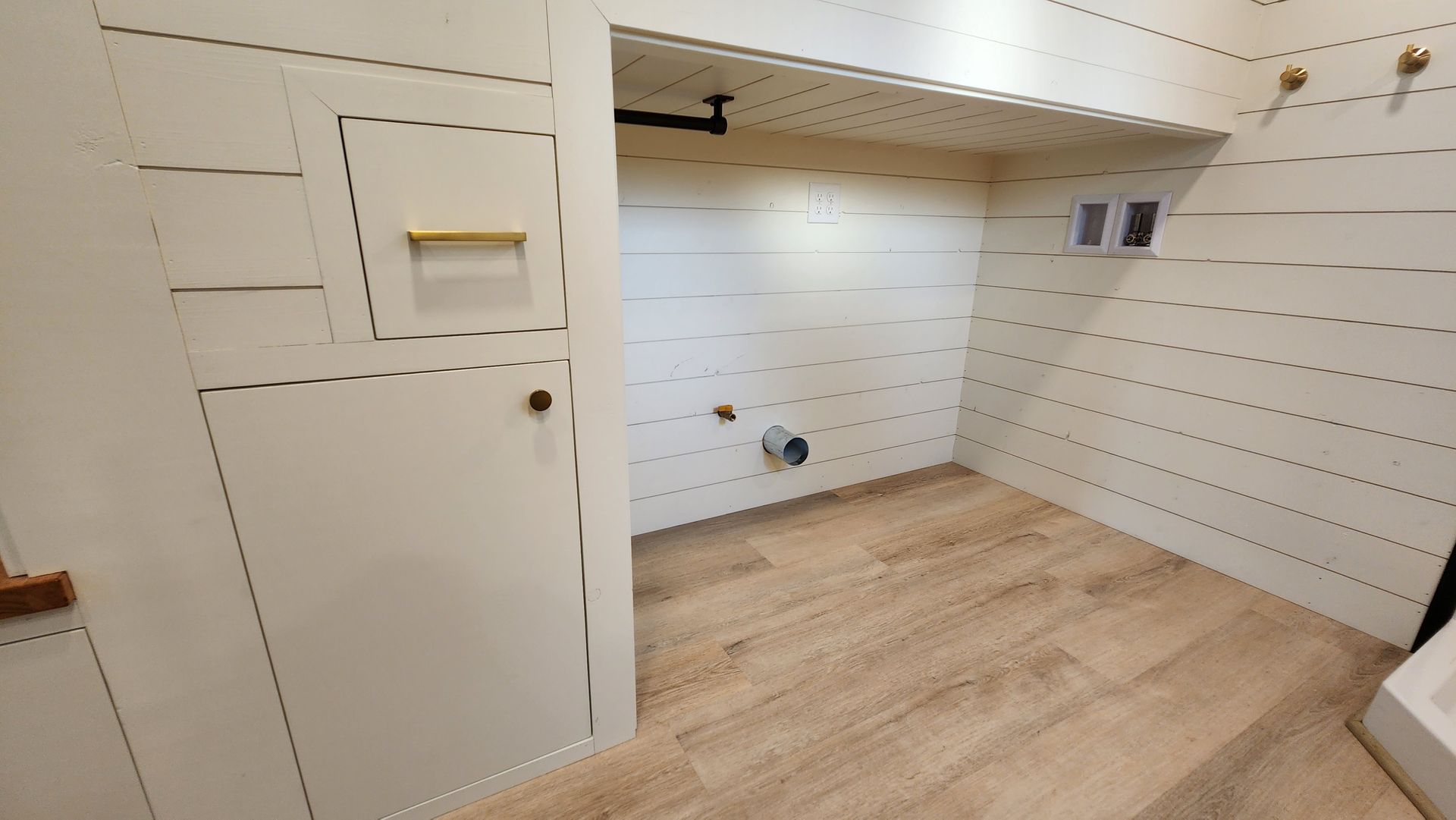 Laundry room with wooden floor, shiplap walls, and plumbing fixtures.