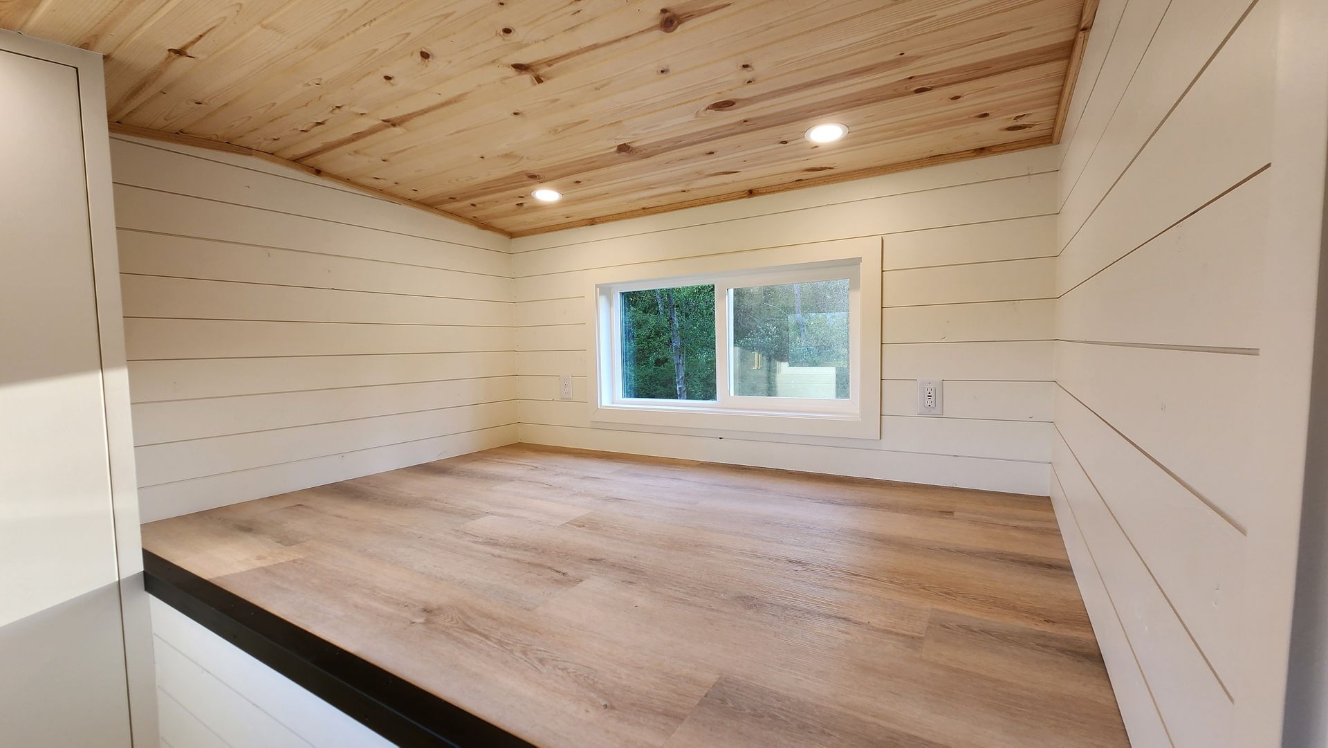Lofted bedroom with wood floor, white walls, window, and wood plank ceiling.