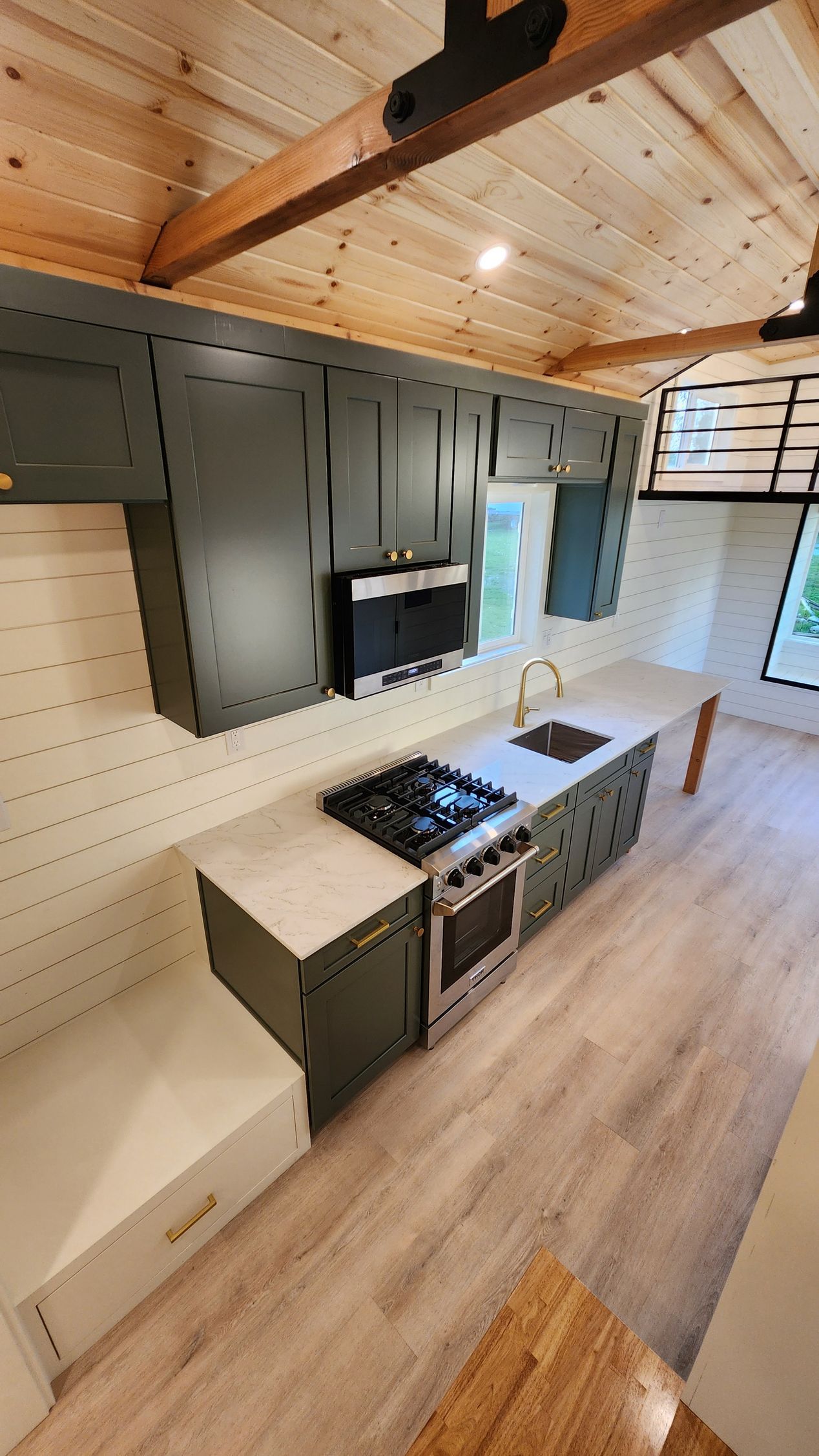 Modern kitchen with dark green cabinets, island with stove, and wood ceiling.