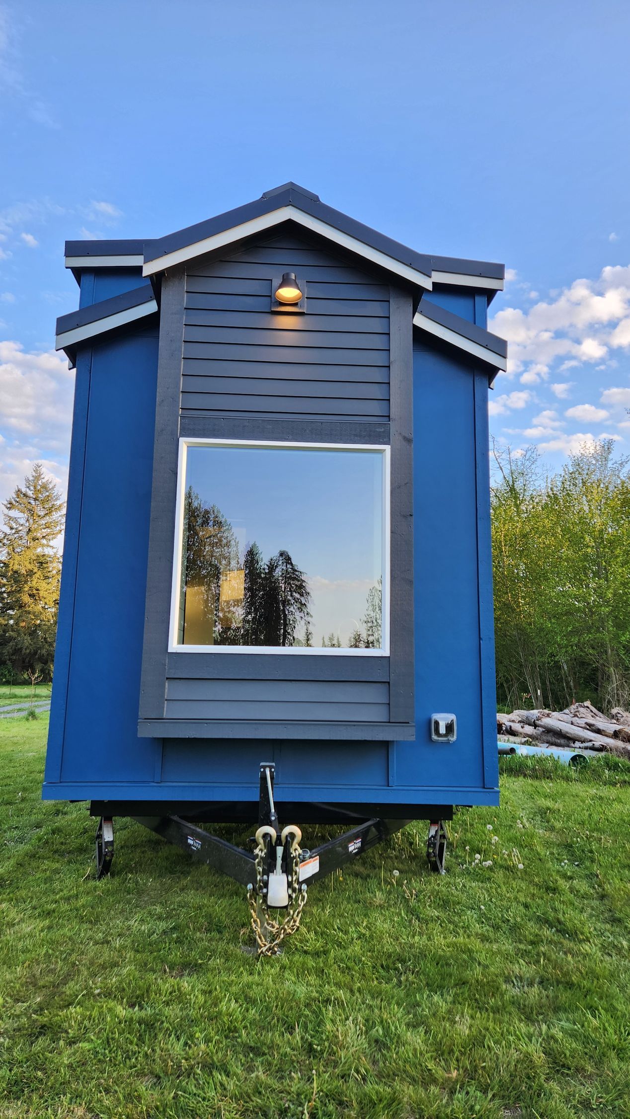 Blue tiny home on wheels with a window and decorative wooden trim.