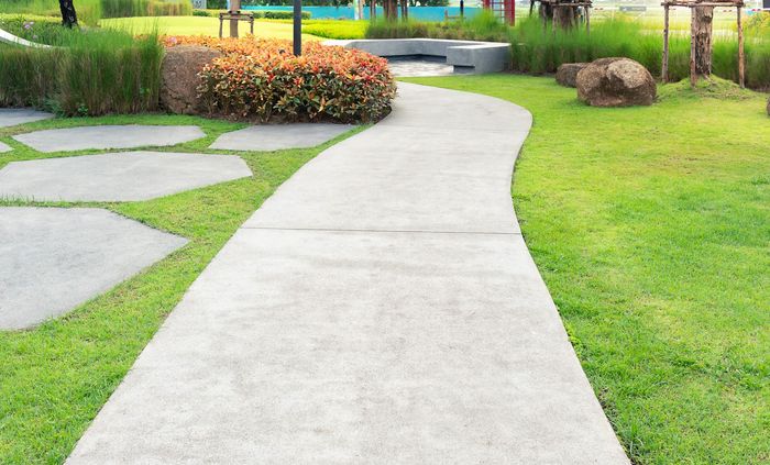 A concrete walkway in a park surrounded by grass and rocks.