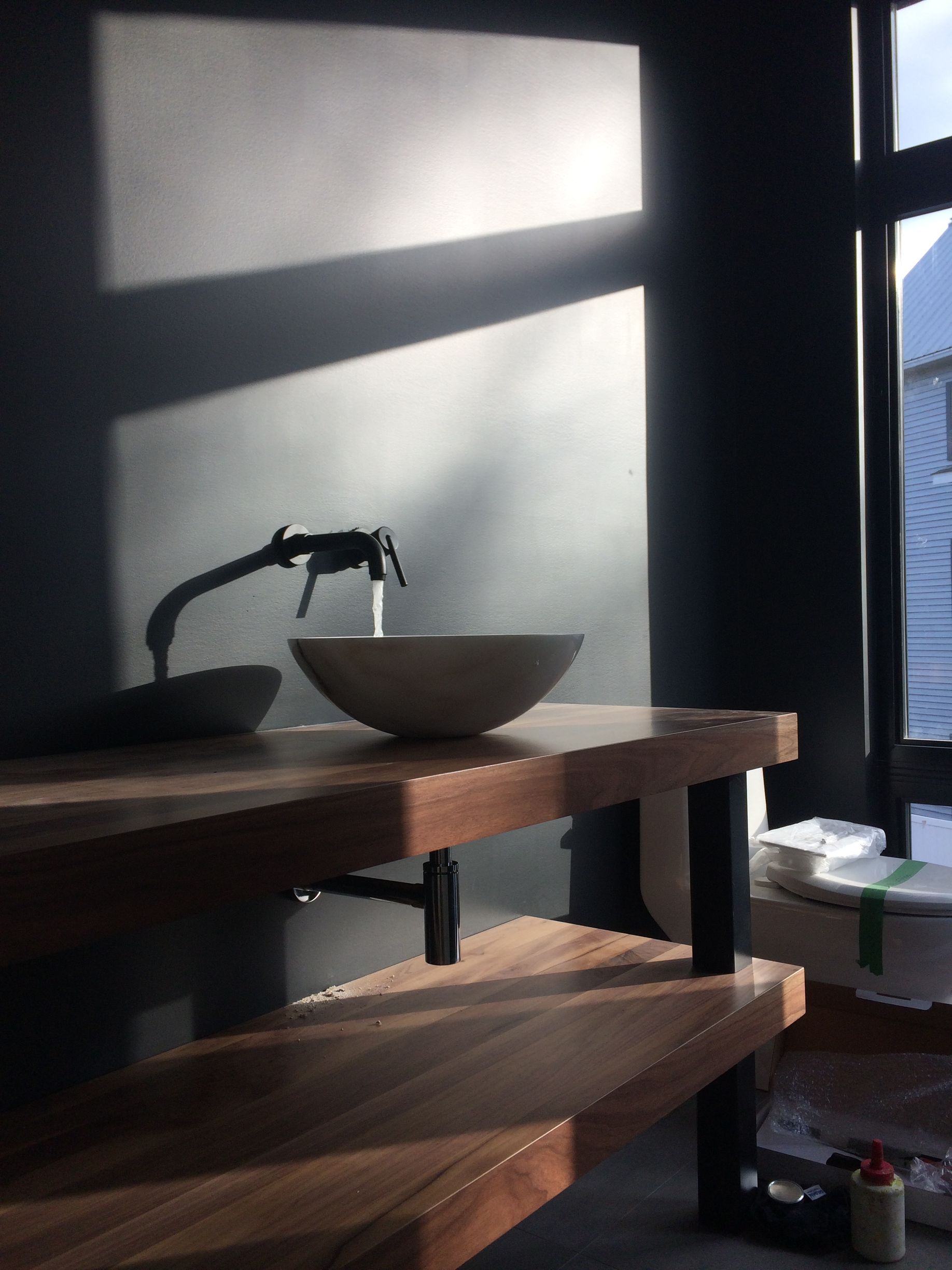 Lavabo de salle de bain moderne avec eau courante, sur un comptoir en bois foncé, éclairé par la lumière du soleil provenant d'une fenêtre.