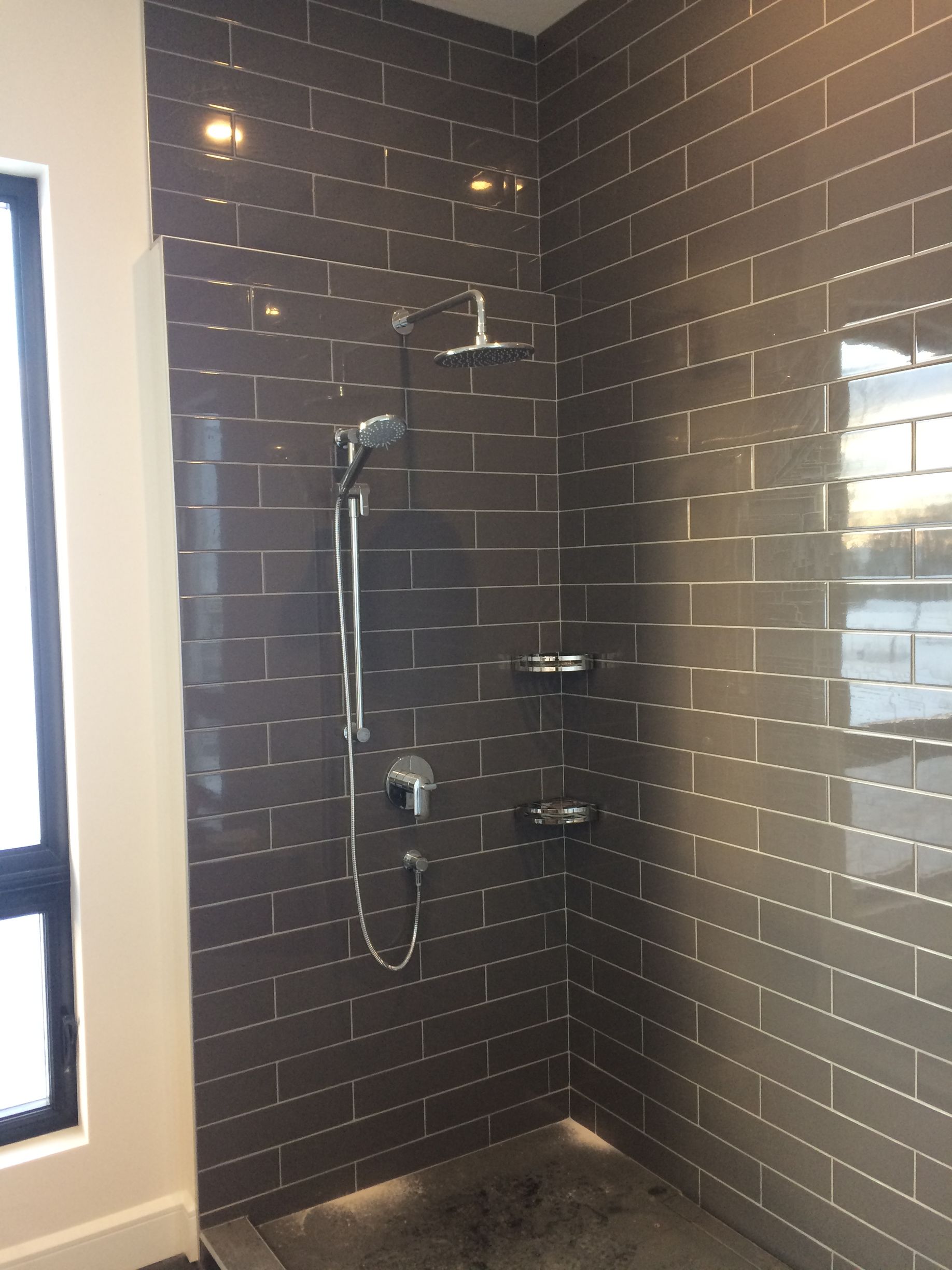 Douche carrelée foncée avec robinetterie et étagères chromées, fenêtre d'angle.