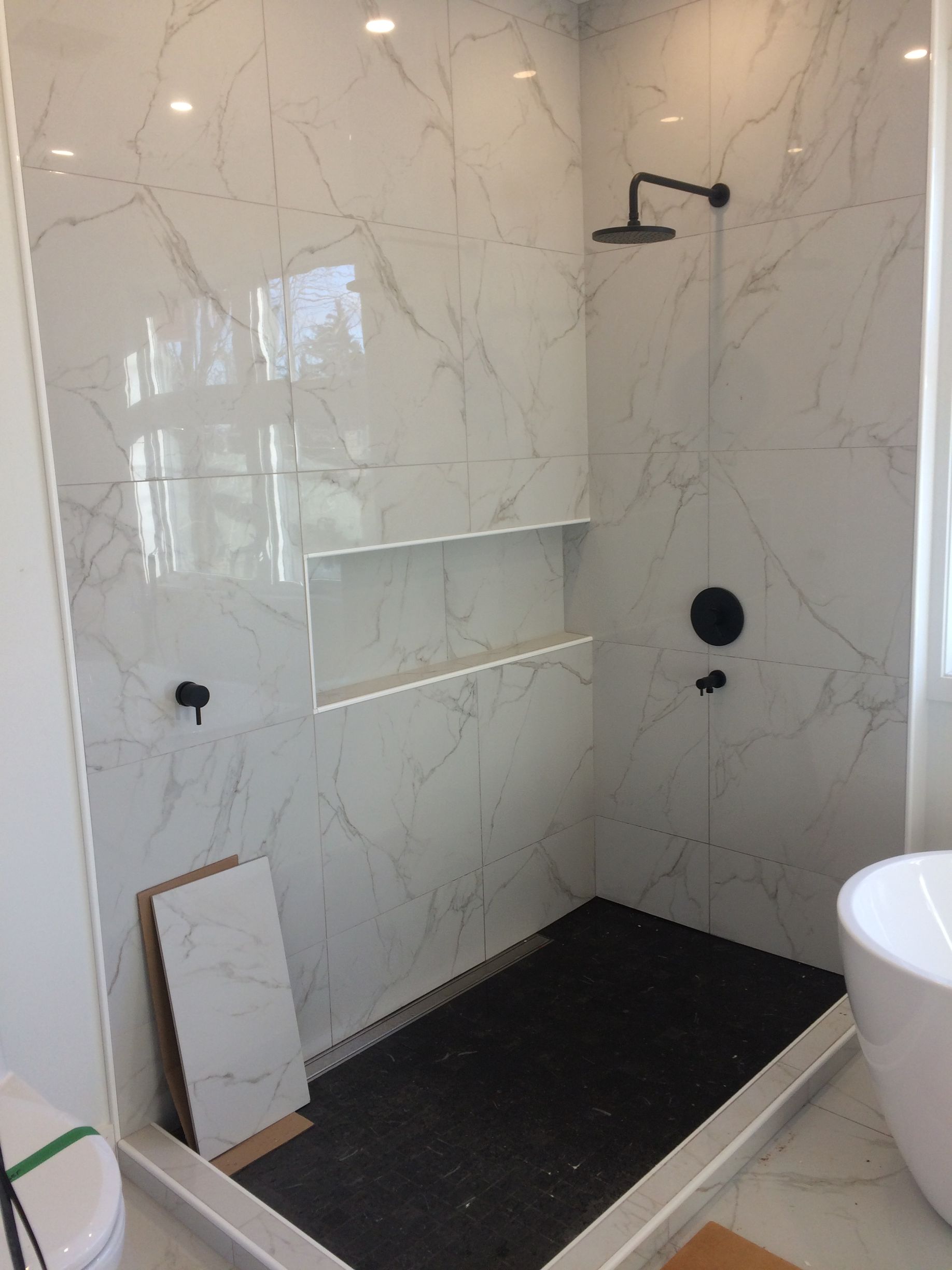 Salle de bains moderne avec douche carrelée en marbre, robinetterie noire et sol de douche carrelé en noir.