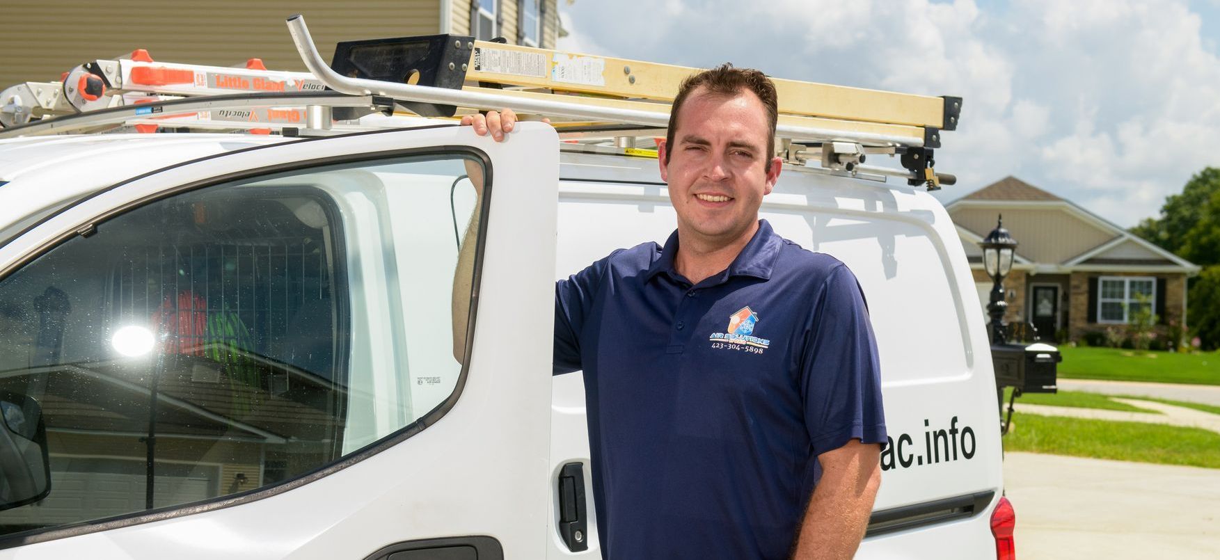 A man is standing in front of a white van with a ladder on the roof.