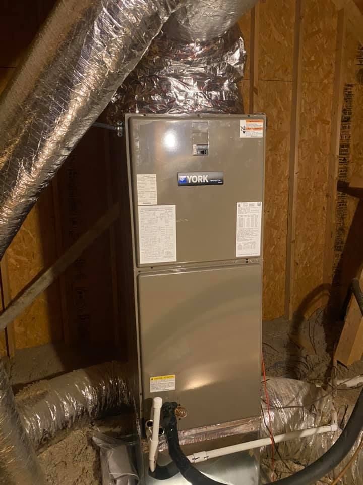 A york air conditioner is sitting in a basement next to a water heater.