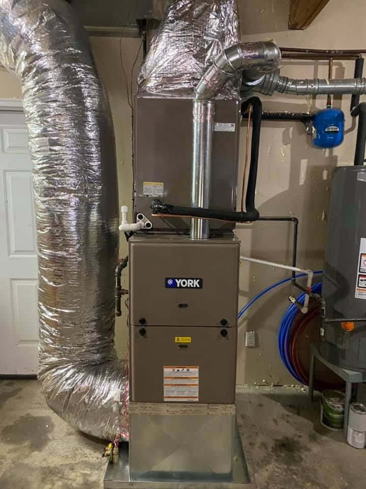 A york air conditioner is sitting in a basement next to a water heater.