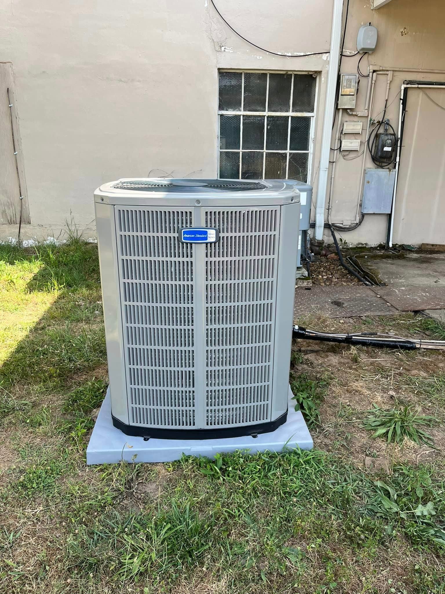 A large air conditioner is sitting in the grass in front of a building.