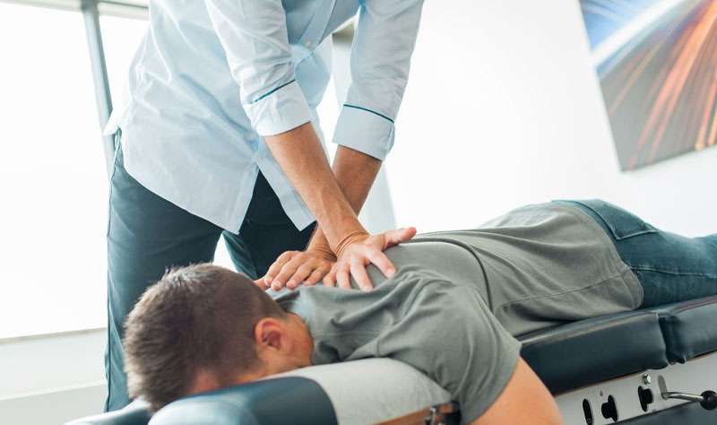 Chiropractor adjusting a patient's back on an examination table.