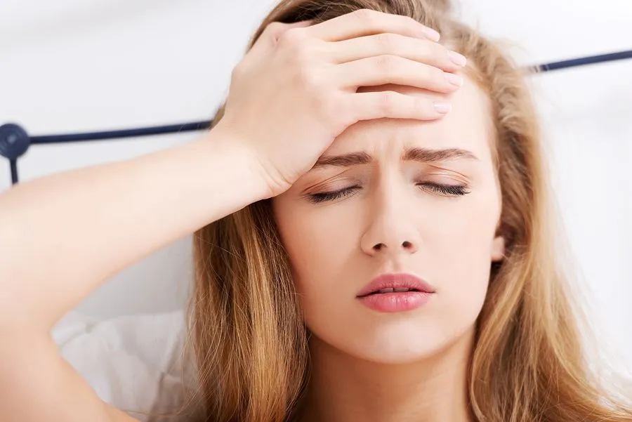 Woman in bed with hand on forehead, eyes closed, appearing to have a headache.