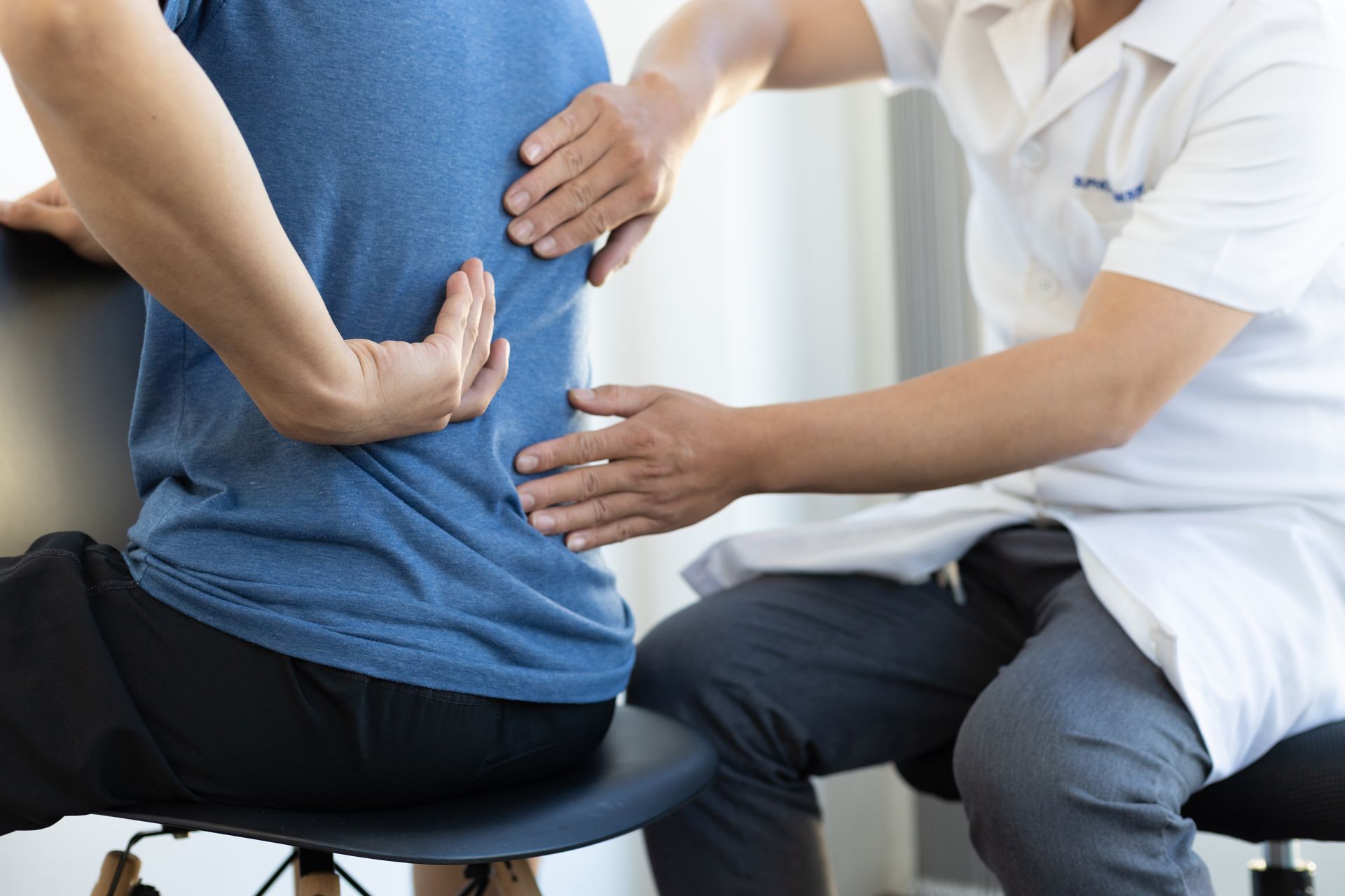 A man is sitting in a chair while a doctor examines his back.