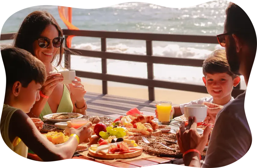 Uma família está sentada à mesa comendo na praia.