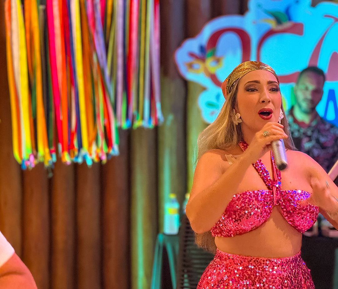 Um homem de camisa azul e chapéu branco está parado em frente a uma parede colorida.