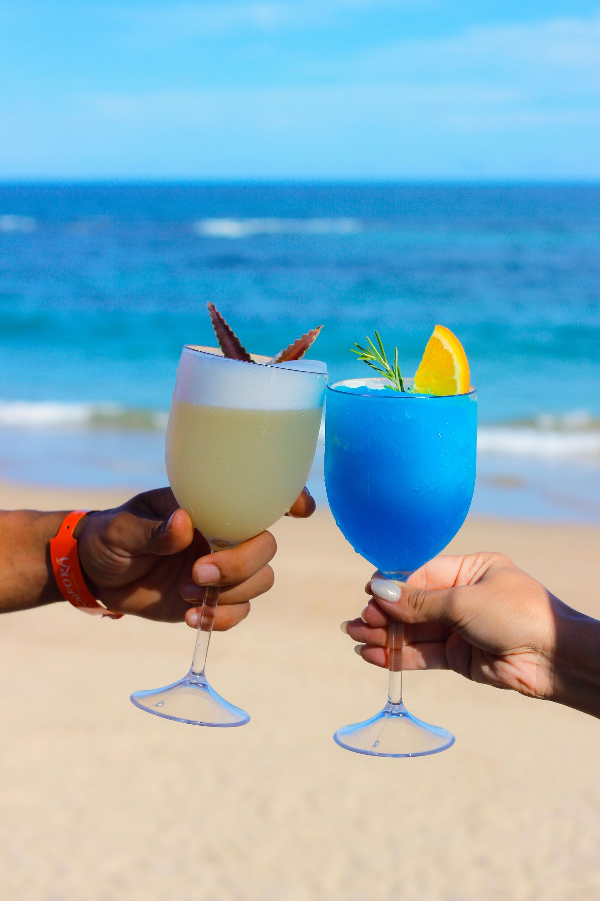 Duas pessoas estão brindando com bebidas na praia.