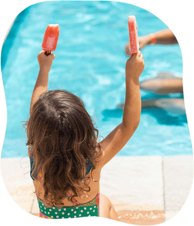 Uma menina está segurando dois picolés em frente a uma piscina.