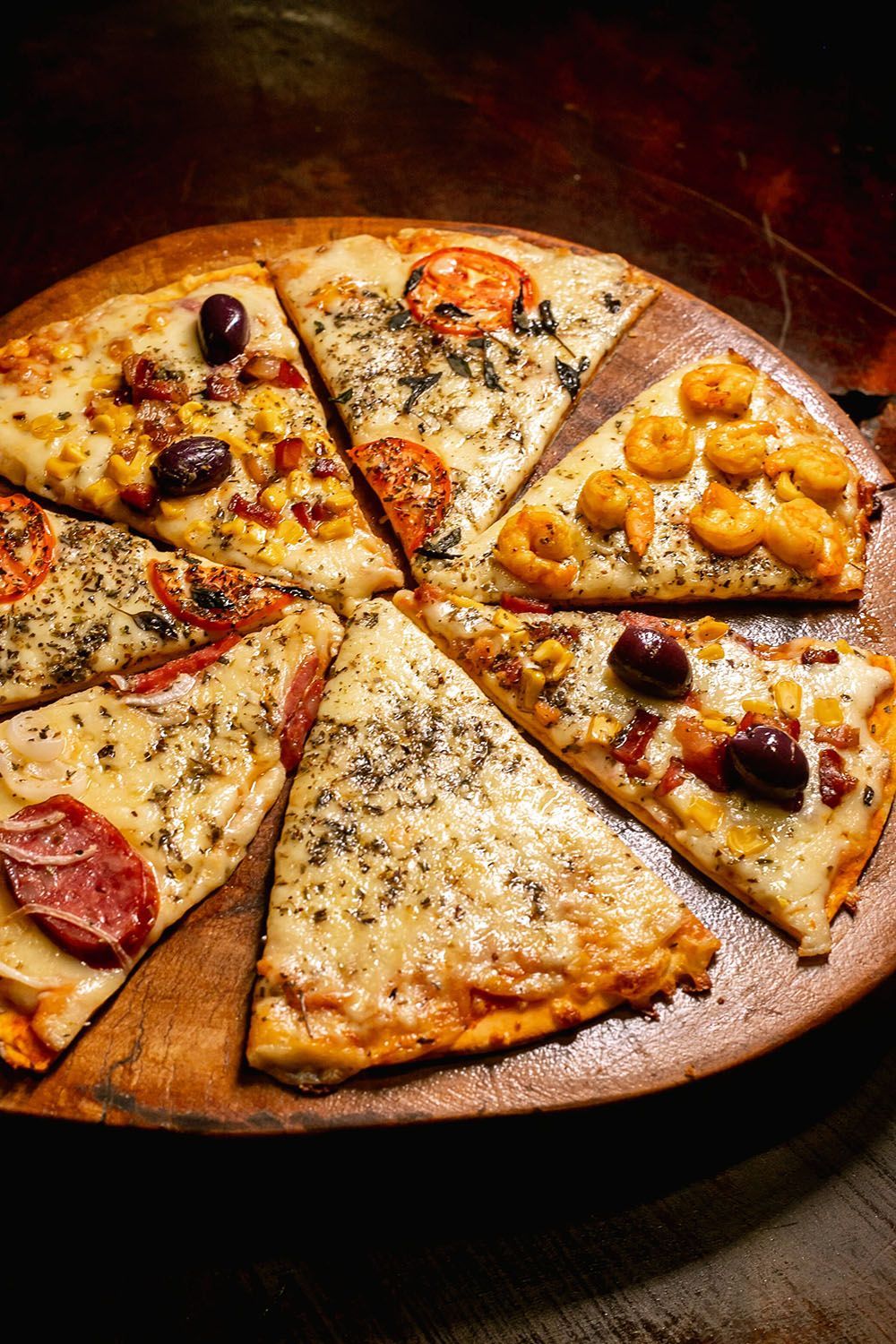Uma pizza com diferentes coberturas está em uma bandeja de madeira.