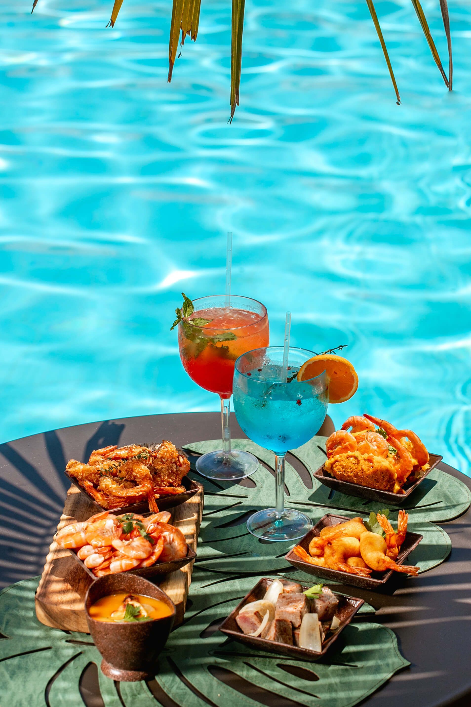 Uma mesa com comida e bebidas ao lado de uma piscina.