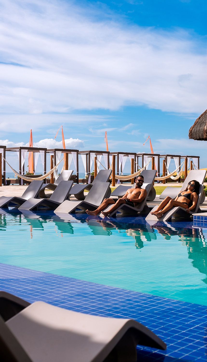 Um homem e uma mulher estão sentados em espreguiçadeiras ao lado de uma piscina.