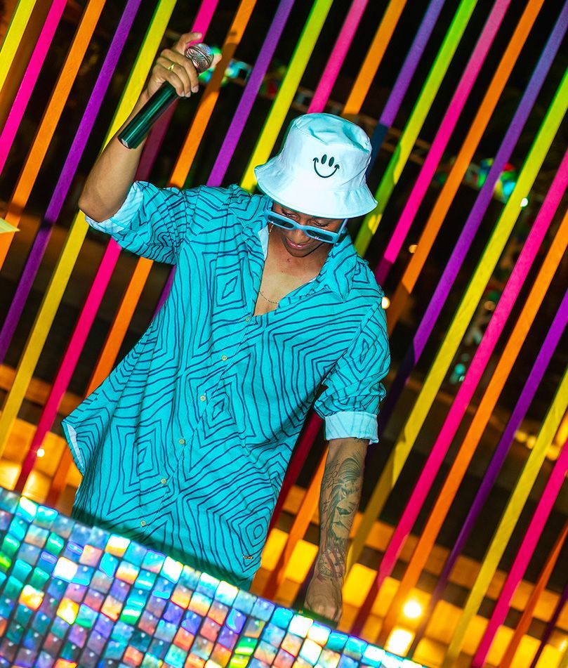 Um homem de camisa azul segura um microfone em frente a uma parede colorida.